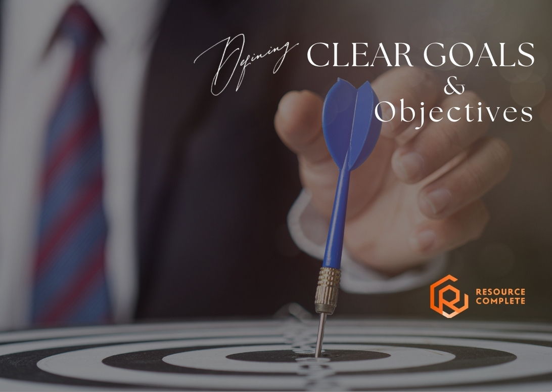 Business professional aiming a dart at the center of a target, symbolizing clear company goals and objectives with Resource Complete branding.