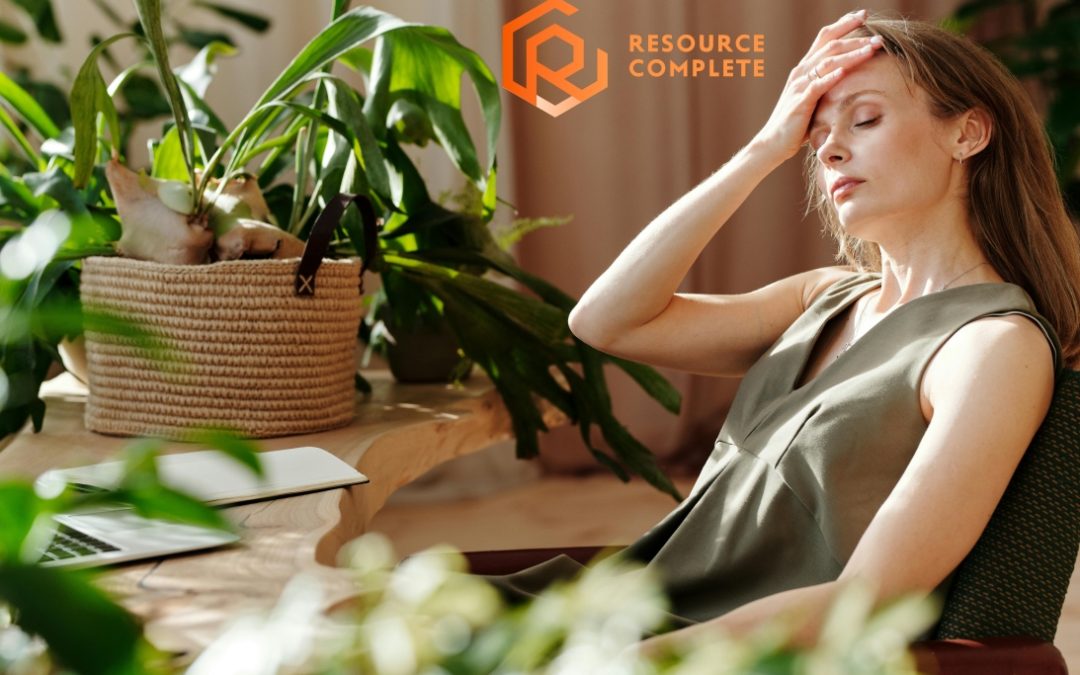 Stressed office worker resting head in hand beside laptop, Resource Complete logo in corner